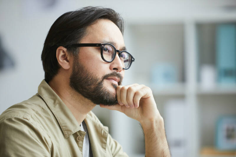 Close-up of serious creative young Asian man with beard being deep in thoughts while working on project in office