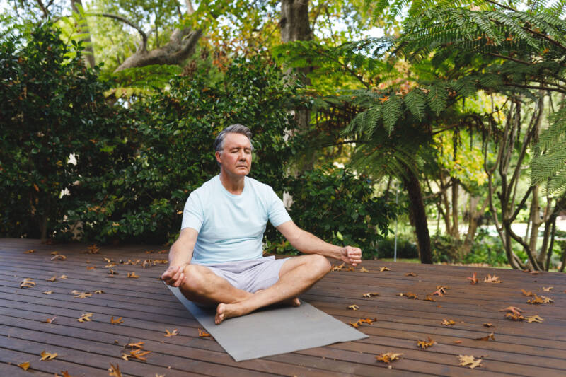 Relaxed senior caucasian man practicing yoga, meditating in garden. healthy retirement lifestyle, spending time self caring at home.